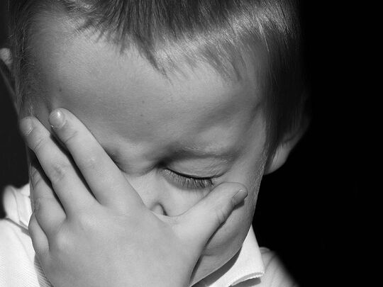 Enfant portant sa main devant son visage, les yeux fermés.